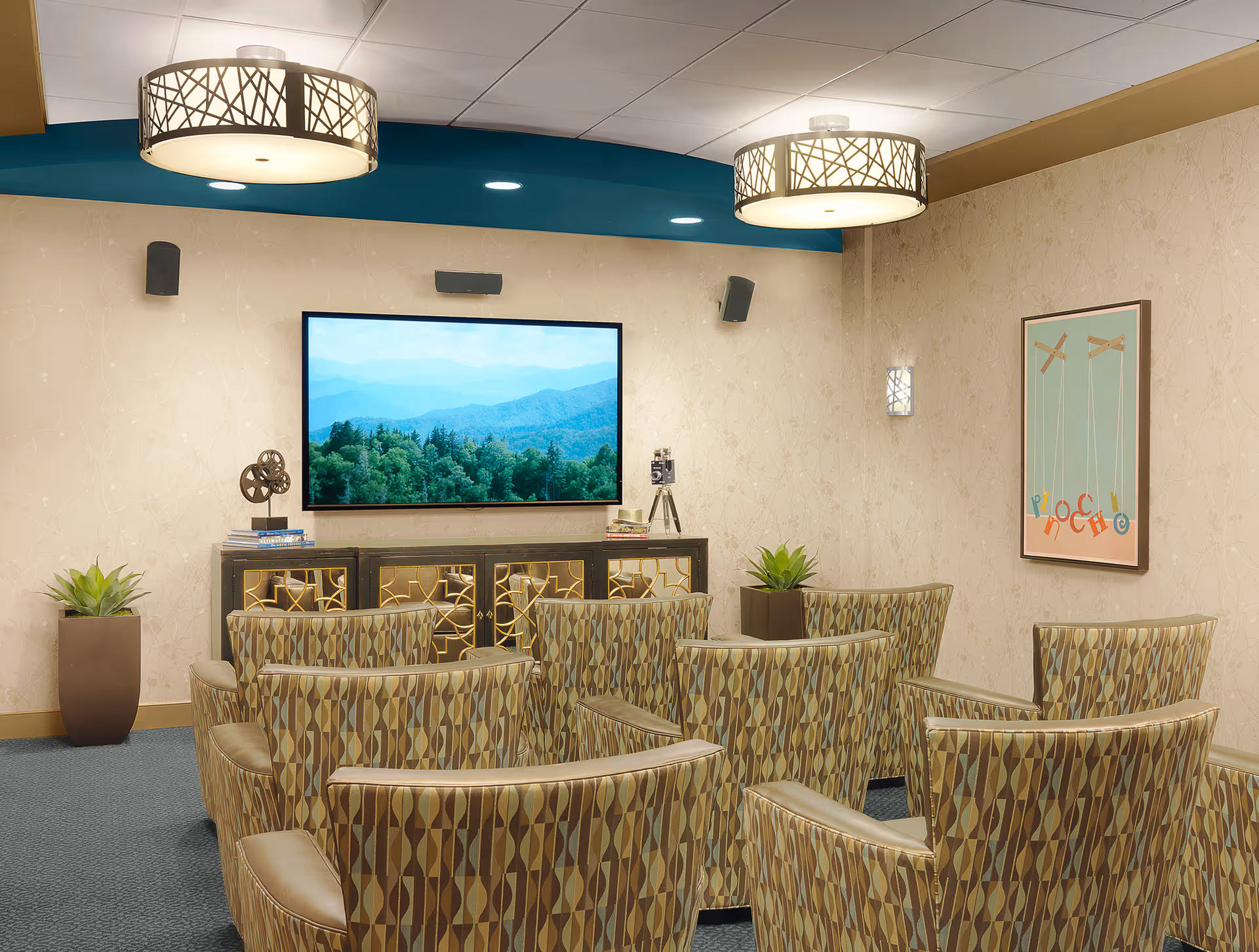 Small screening room with patterned armchairs facing a wall-mounted TV, decorative cabinet, potted plants, and pendant lights.