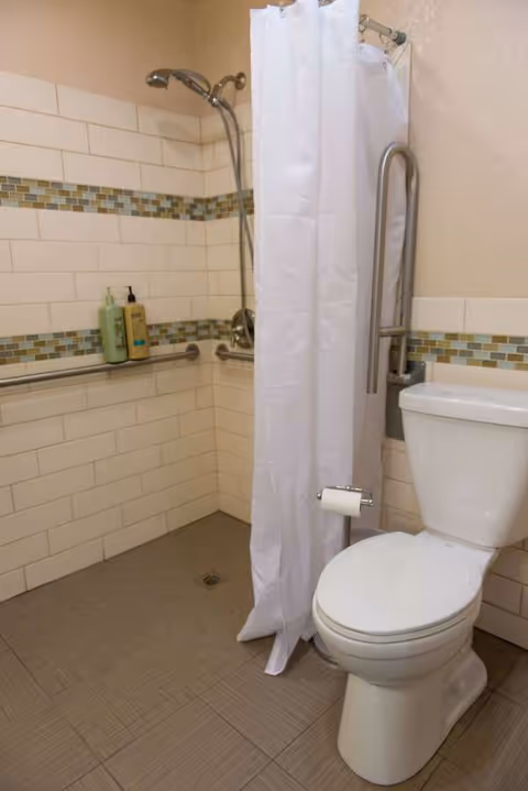 Accessible bathroom with shower, grab bars, toilet, and tiled walls in a senior facility.