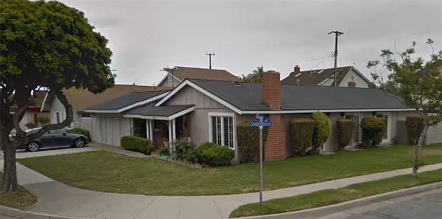 Single-story senior living facility with manicured lawn, shrubs, and a street corner in front.