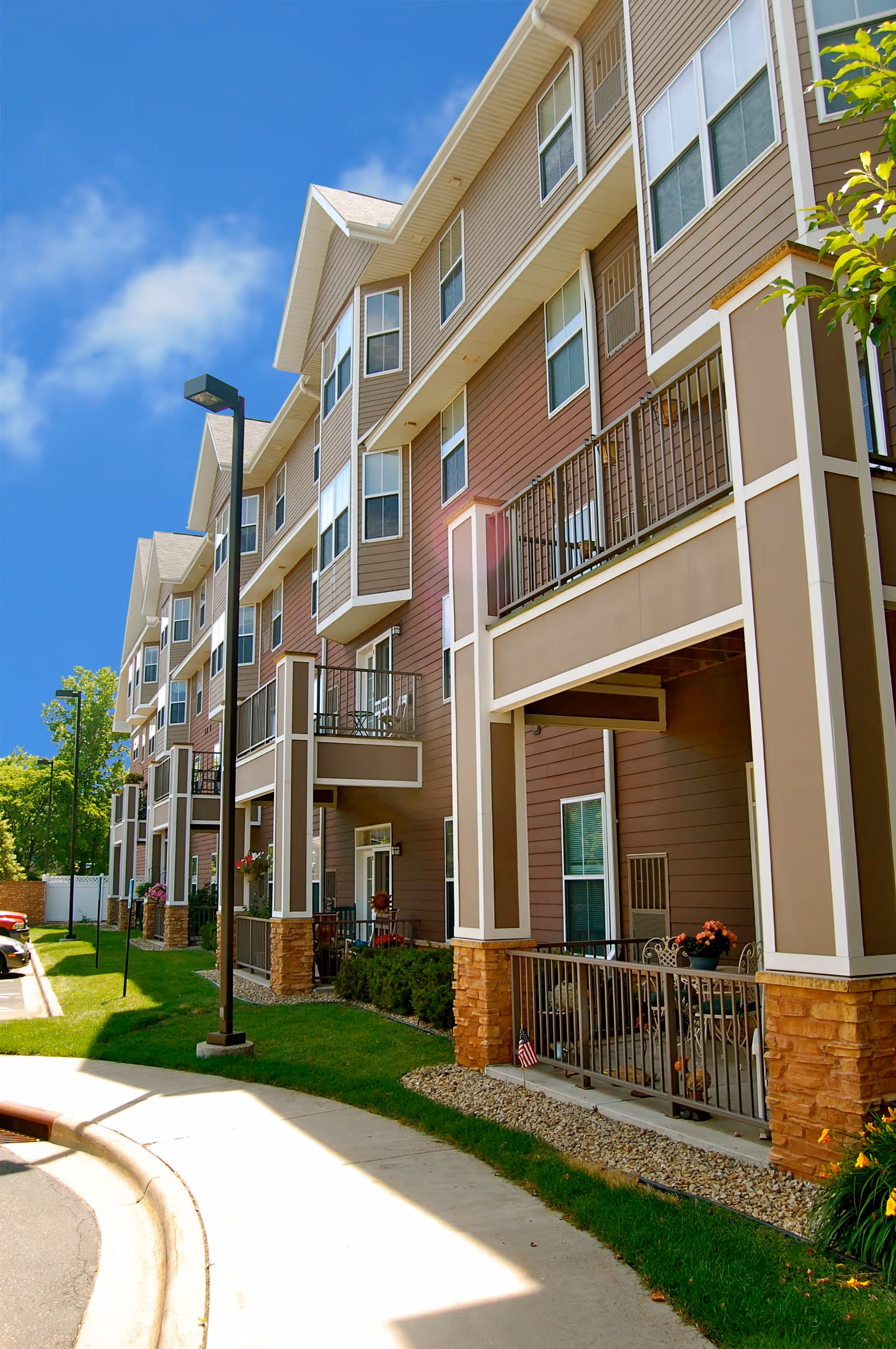 Exterior view of a multi-story residential building with balconies and a well-maintained lawn under a clear blue sky.