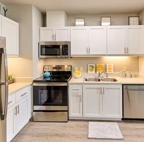 Bright modern kitchen with white cabinets, stainless steel appliances, a double sink, and a stove with a teal kettle.