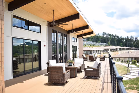Covered outdoor deck with wicker chairs and tables overlooking neighboring buildings and trees.