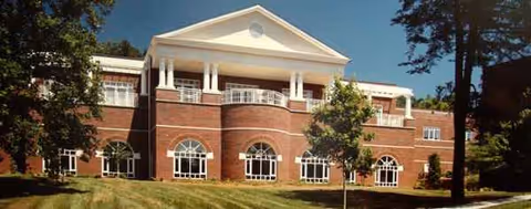 Brick senior living facility with white columns and arched windows, on a green lawn.