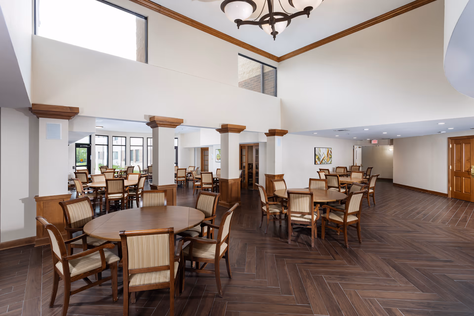 Spacious dining room with multiple round wooden tables and chairs under a high ceiling.