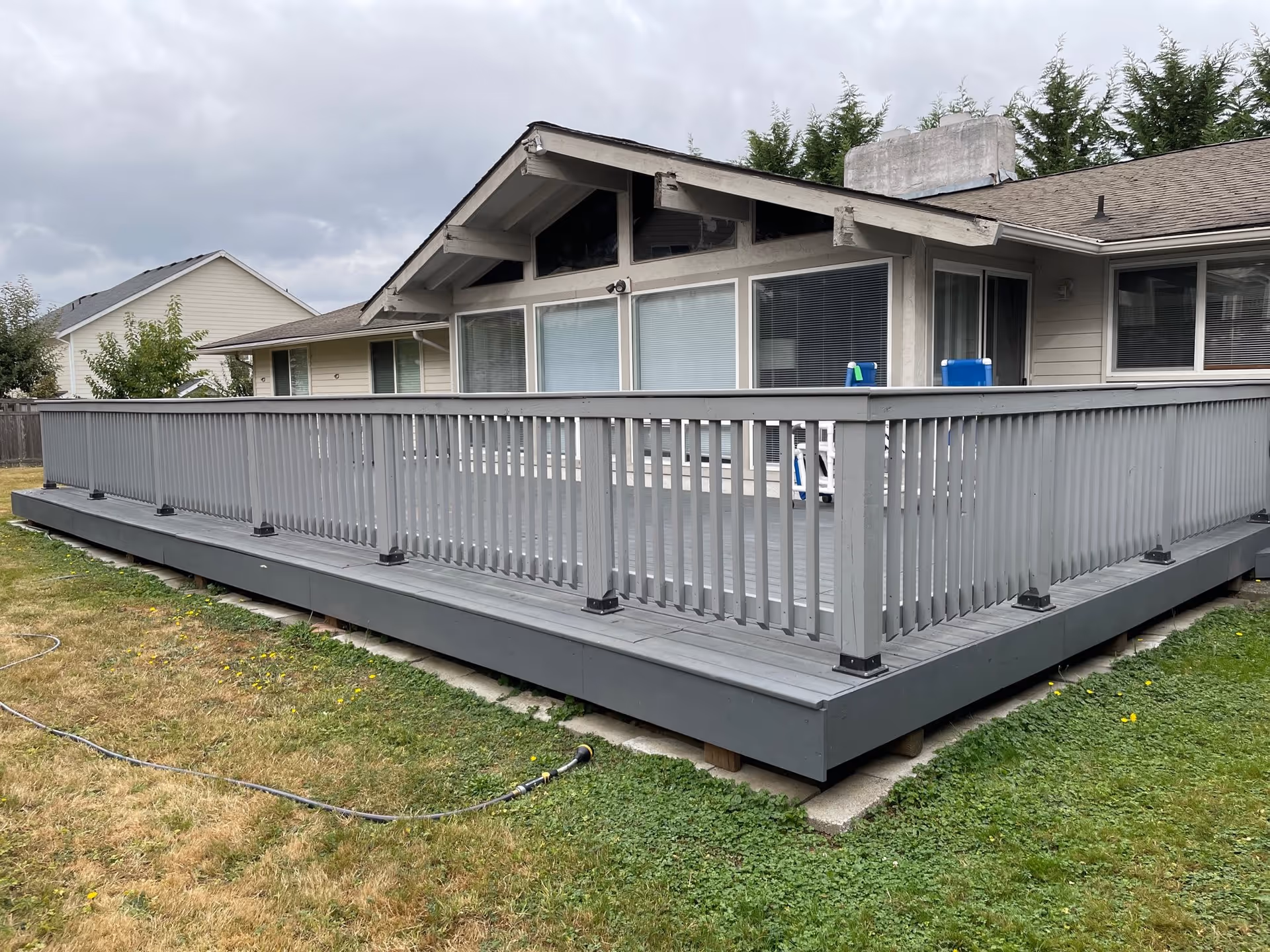 Gray wooden deck with railing attached to a single-story house overlooking a grassy yard.