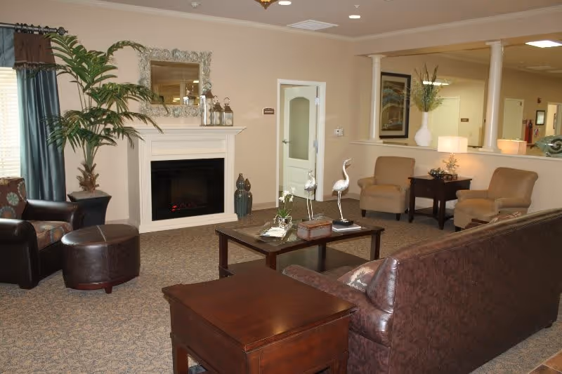 A cozy senior living lounge with a leather sofa and chairs arranged around a coffee table in front of a fireplace.