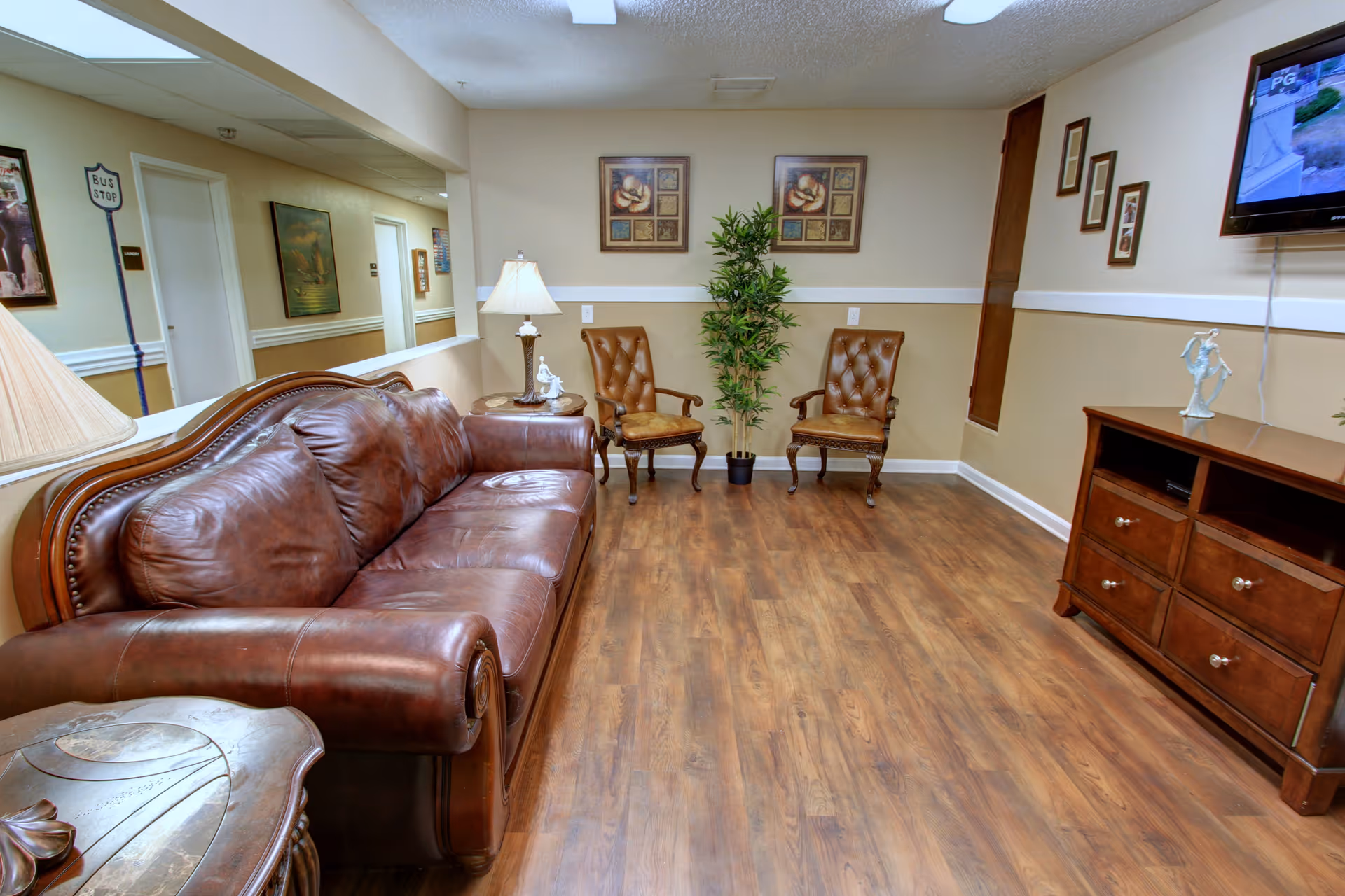 A furnished common living room with a brown leather sofa, two armchairs, a TV console and wood floors.