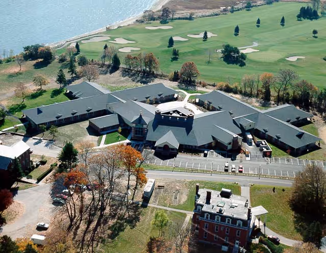 Aerial view of a sprawling multi-wing rehabilitation facility beside a golf course and waterfront.