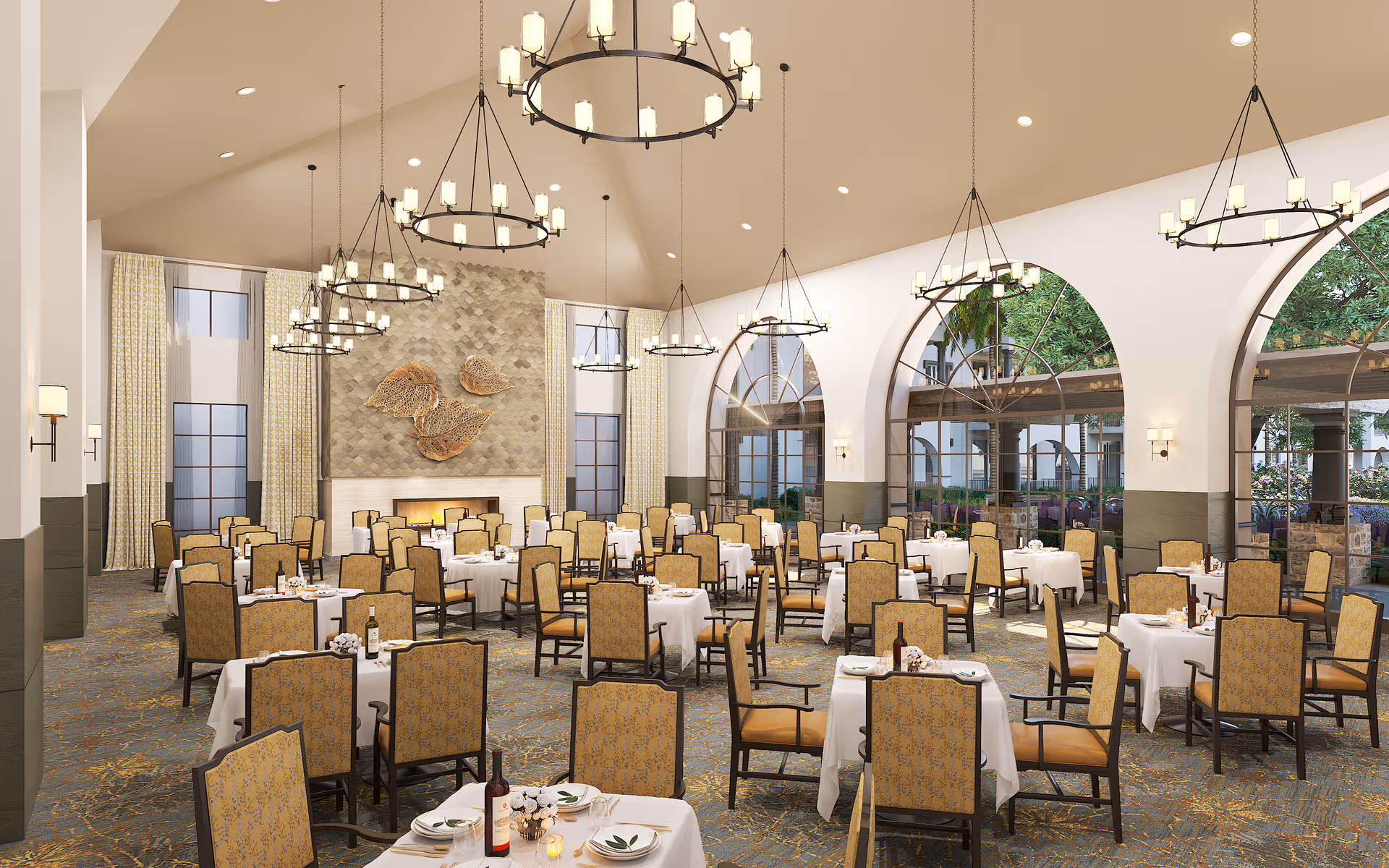 Spacious elegant dining room with white-clothed tables, upholstered chairs, large chandeliers, arched windows, and a fireplace.
