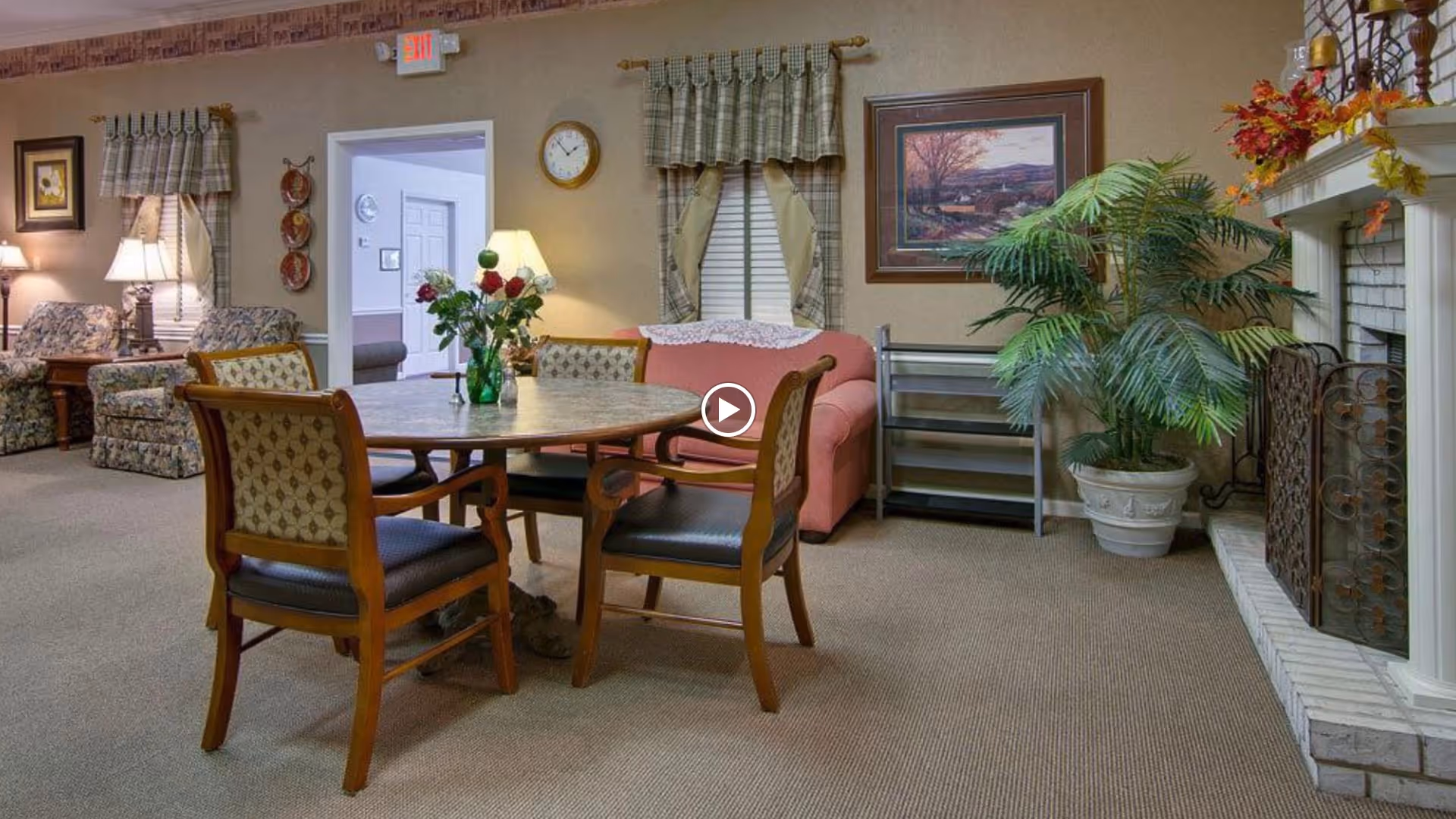 A cozy communal living room with a round table and chairs in front of sofas, a fireplace, and decorative plants.