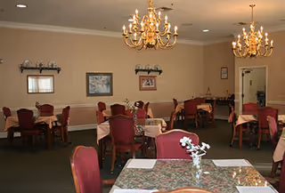 Formal dining room with multiple tables covered in tablecloths, red upholstered chairs, and chandeliers.