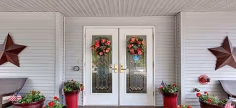 Double glass doors with wreaths welcome visitors, flanked by potted plants on a porch.