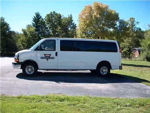 White passenger van with Rocky Ridge Manor logo parked on a driveway near trees