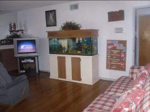 Living room in a senior facility featuring a large fish tank on a cabinet and TV.
