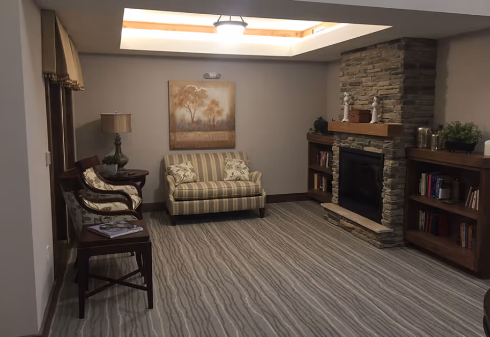 Cozy living room with a striped loveseat, two armchairs, bookshelves, and a stone fireplace beneath a skylight.