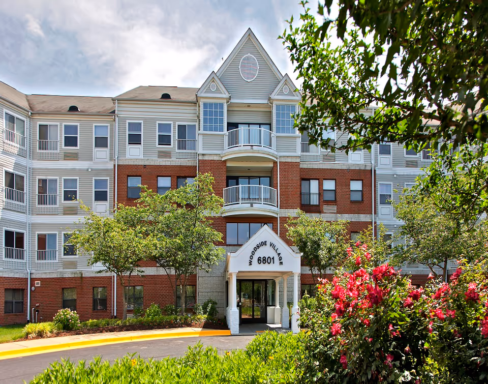 Front view of Woodside Village senior living building with landscaped entrance and blooming bushes