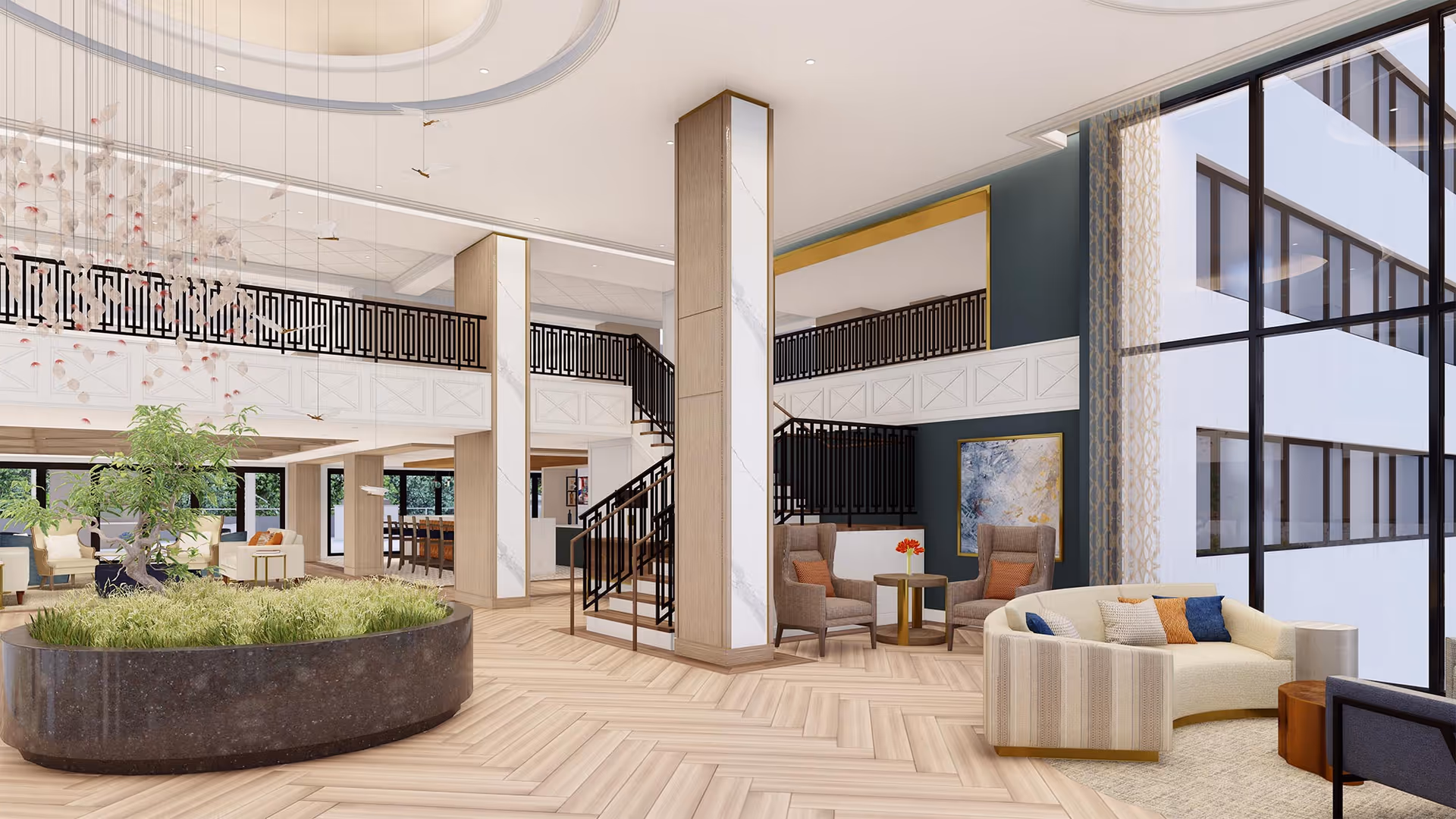 Spacious and modern senior living facility common area with large windows, a curved beige sofa with colorful pillows, two armchairs with a small round table, a large planter with greenery, and a staircase leading to an upper level with black railings.