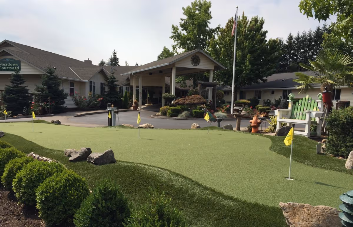 Entrance of Meadows Courtyard senior living facility with a landscaped putting green and covered porte-cochere.