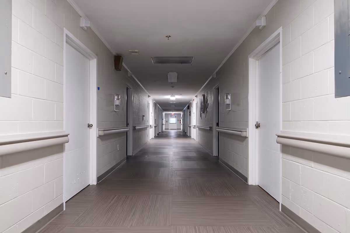 Long empty interior hallway in a senior living facility with doors and handrails.