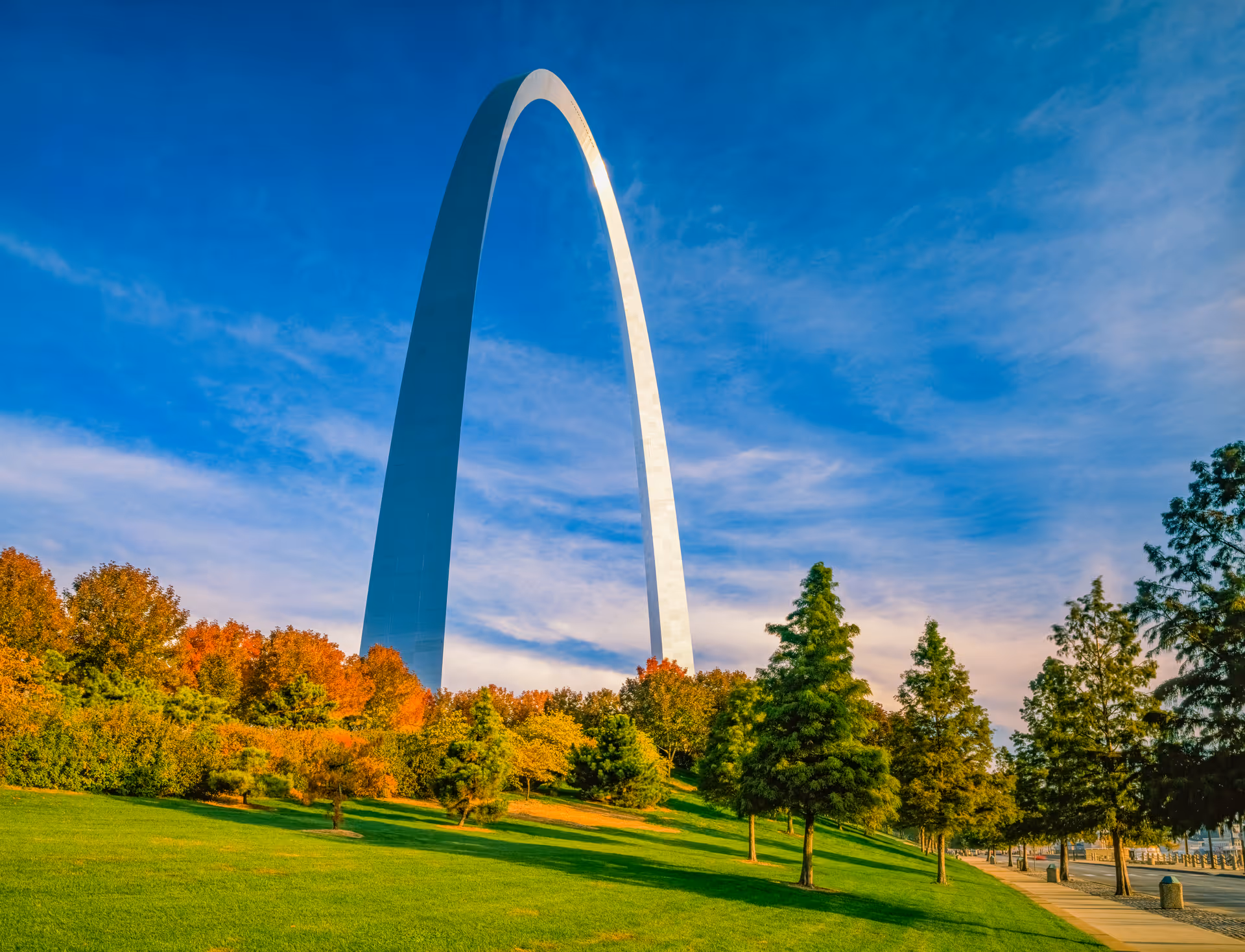 The Gateway Arch towering over a green park with trees under a blue sky.