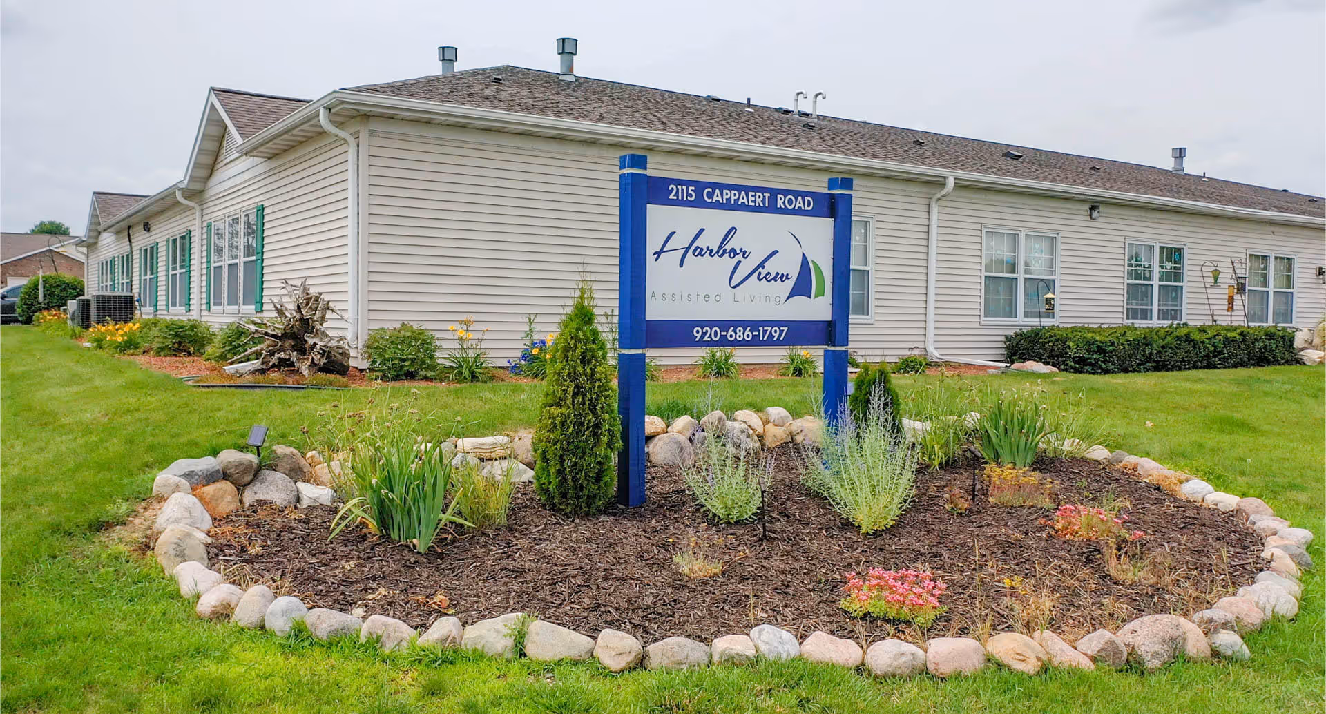 Front exterior of Harbor View Assisted Living with a blue sign, landscaped flower bed, and the single-story building.