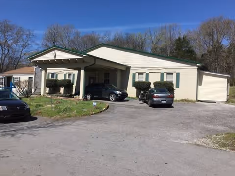 Single story senior living facility with a covered entrance and cars parked in front.