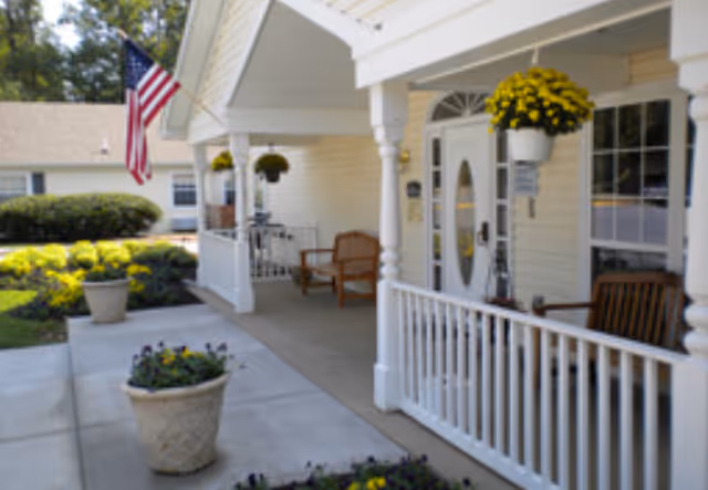 Exterior view of Arden Courts Silver Spring porch with chairs, hanging flowers, and an American flag.