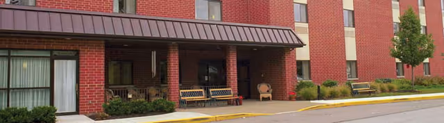 Covered brick building entrance with benches and small landscaped beds along the sidewalk.