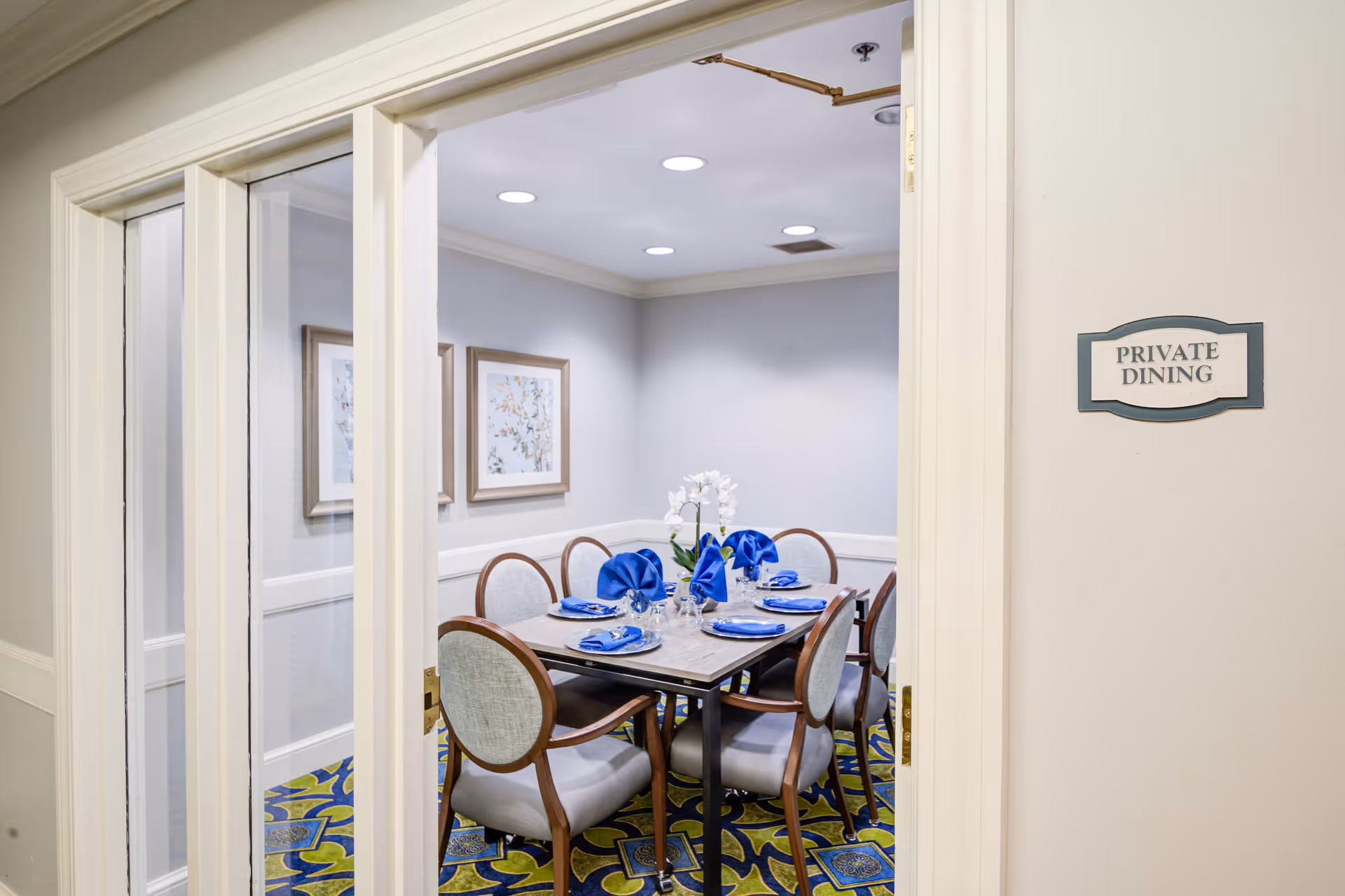 View through a doorway into a private dining room with a table set for six, blue napkins, and a floral centerpiece.