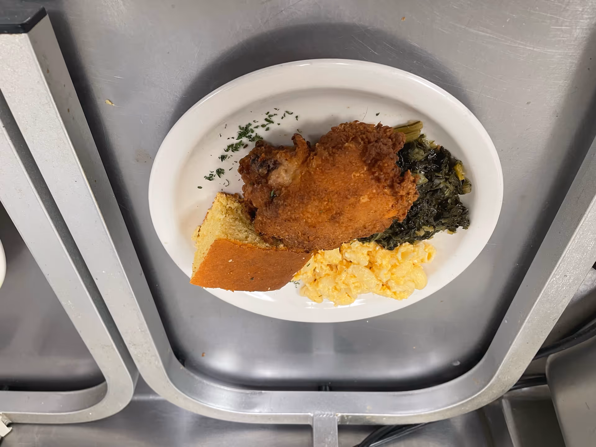 A plate with fried chicken, cornbread, collard greens, and macaroni and cheese on a metal tray.