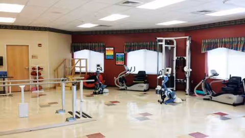 Interior gym at a senior living center with exercise machines and a ballet barre.