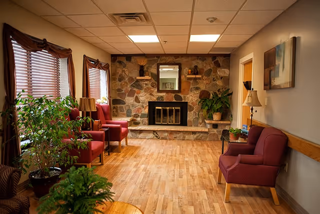 Cozy common sitting room with a stone fireplace, hardwood floors, potted plants, and upholstered armchairs.