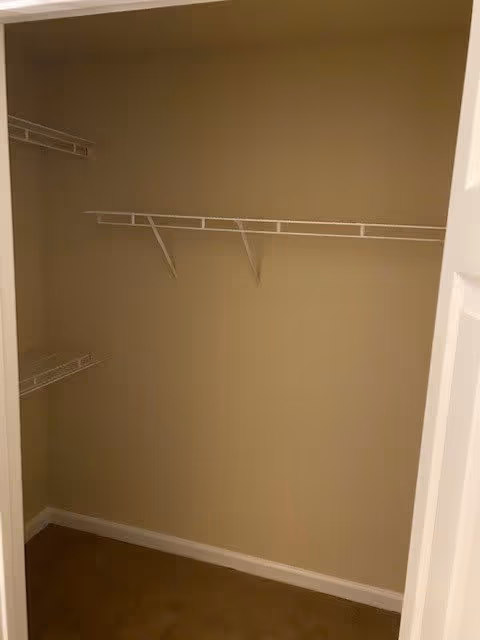 Empty closet with beige walls, white wire shelving, and brown carpet.