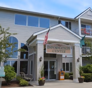 Exterior view of The Vintage at Mount Vernon Information Center entrance with a covered porch, American flag, potted plants, and large windows on a sunny day.