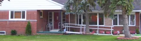 Front view of a single-story brick senior living facility with a wheelchair ramp and lawn.