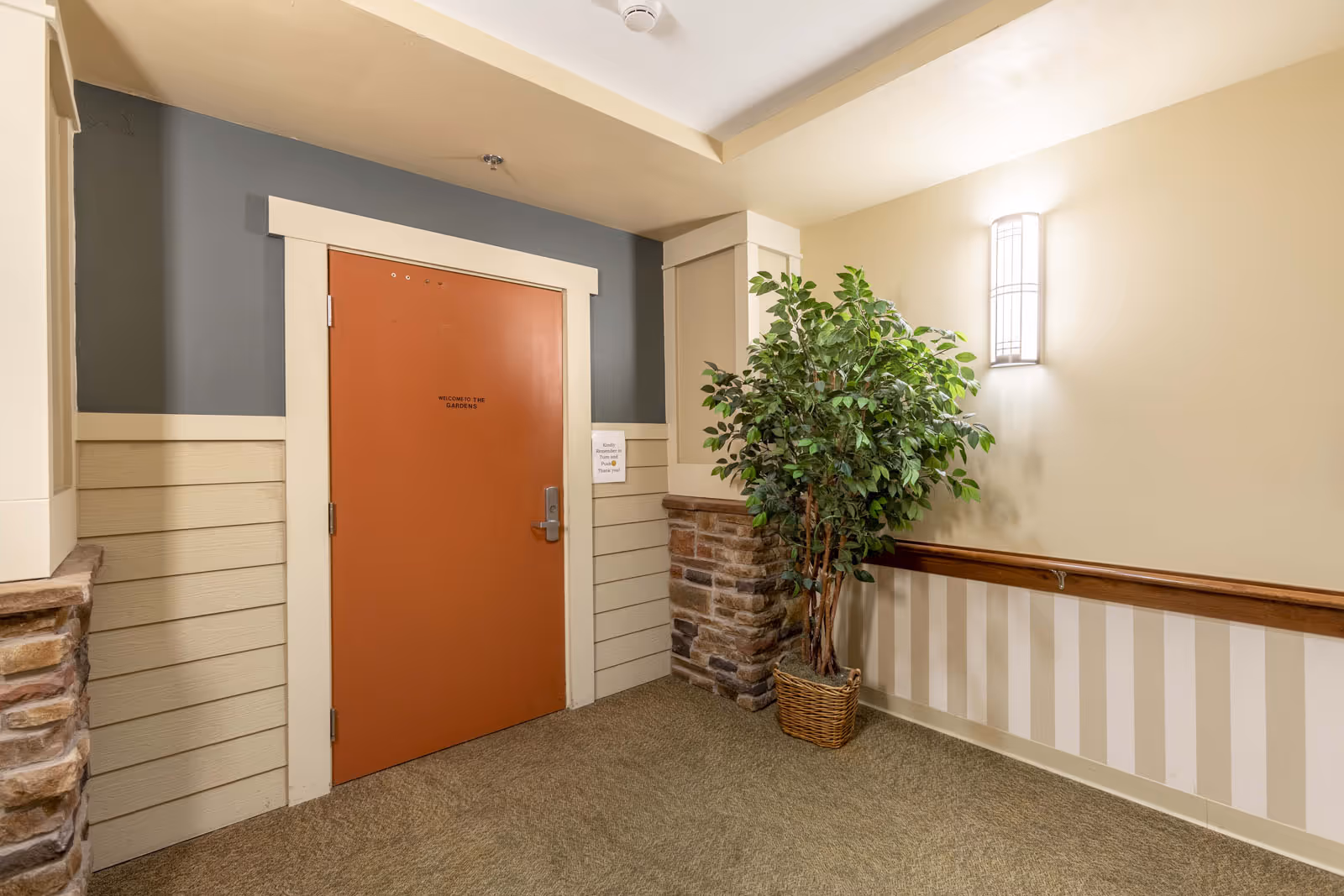 Interior hallway with an orange door, a potted plant, a wall sconce, and wood-and-stone trim.