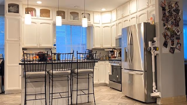 Bright kitchen with white cabinetry, a center island with three bar stools, pendant lights, and stainless steel refrigerator and stove.