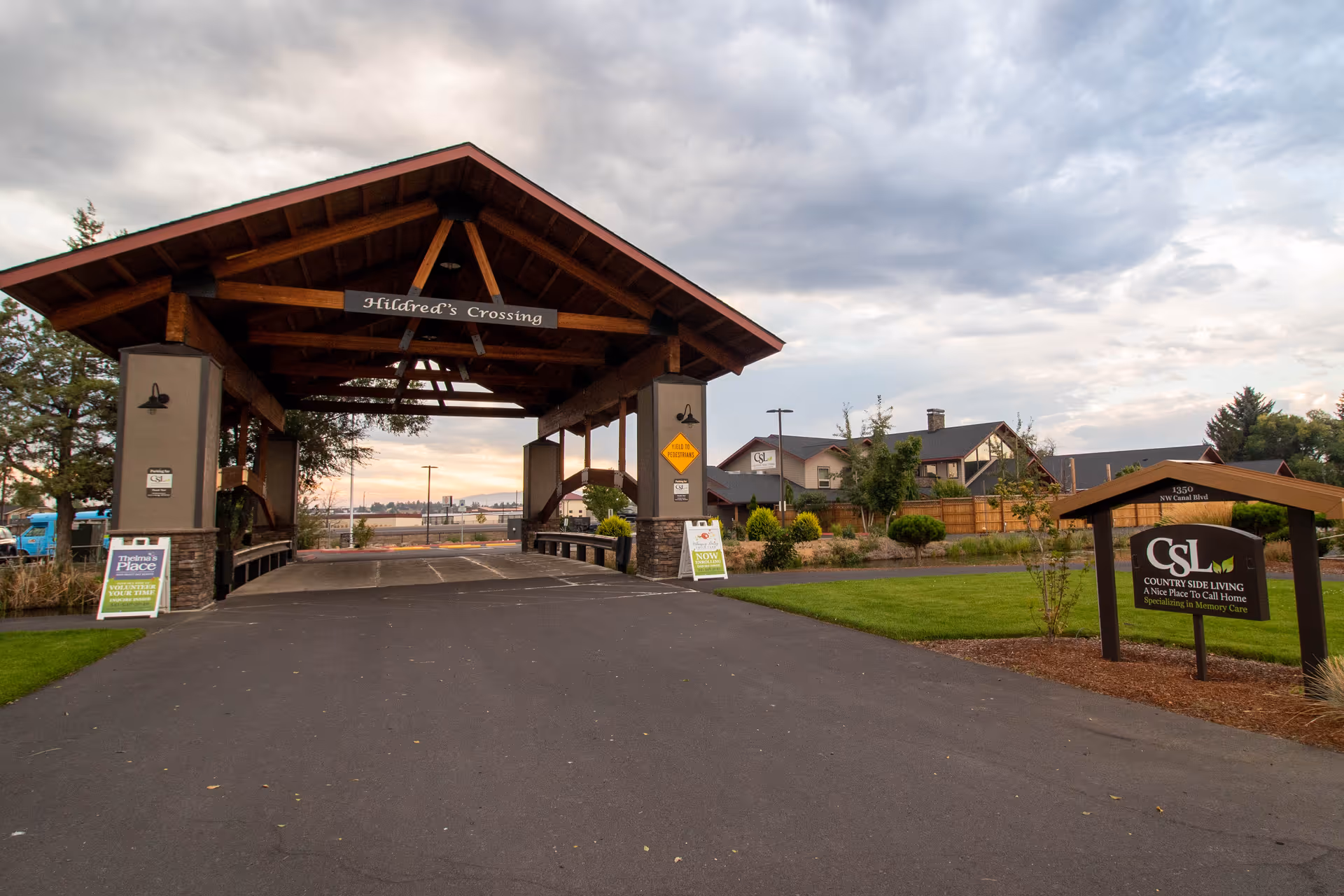 Entrance to Country Side Living - Memory Care facility featuring a large wooden covered driveway labeled 'Hildred's Crossing' with landscaped greenery and a sign displaying the facility name and address.