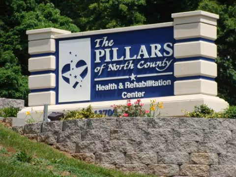 Blue sign reading The Pillars of North County Health & Rehabilitation Center on a stone wall