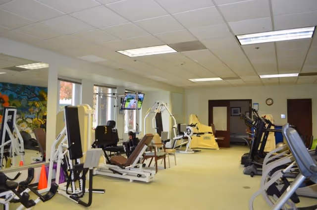 Interior fitness room with treadmills, weight machines, and exercise equipment in a bright senior living facility.