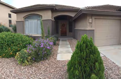 Front view of a single-story home with a walkway, shrubs, and a two-car garage.