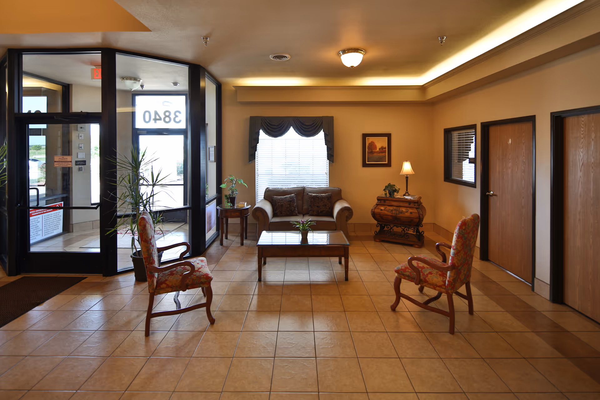 Well-lit nursing center lobby with a sofa, two upholstered chairs around a coffee table, side tables and glass entrance doors.
