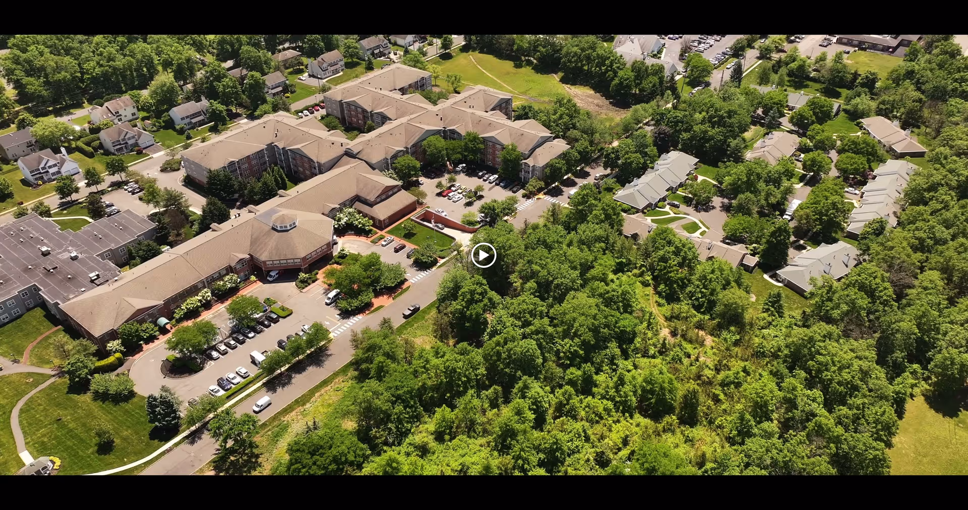 Aerial view of a large senior living facility named Laurel Circle surrounded by trees and greenery, with multiple buildings, parking lots, and nearby residential houses.