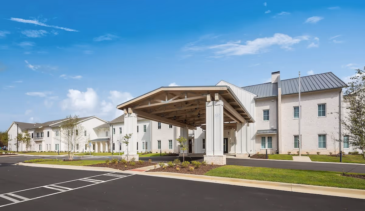 Wide front view of a two-story senior living building with a large covered porte-cochere entrance and surrounding driveway.