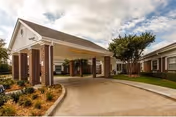 Covered porte-cochere entrance of a brick-and-siding senior living building with a circular driveway and landscaped grounds.