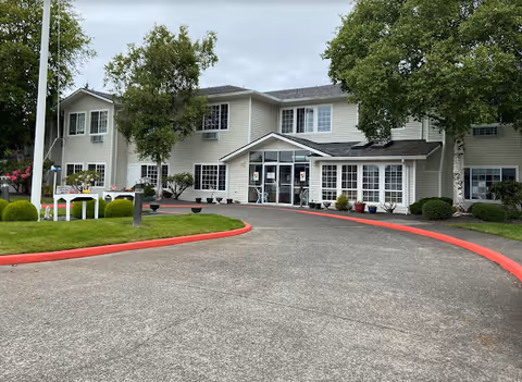 Front exterior of a two-story senior living building with a circular driveway, entrance canopy, and landscaped grounds.
