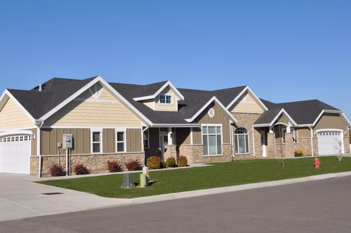 Single-story suburban-style building with stone and siding facade, attached garages, and a manicured lawn under a clear blue sky.