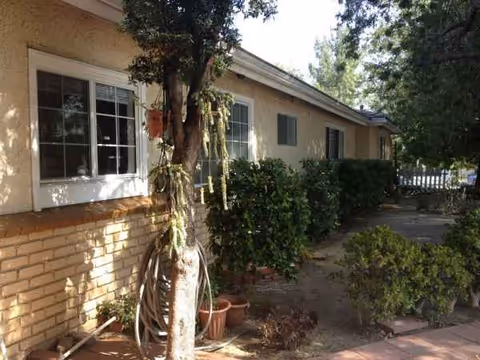 Exterior view of Angels of the Valley Board and Care with plants and hoses near windows.