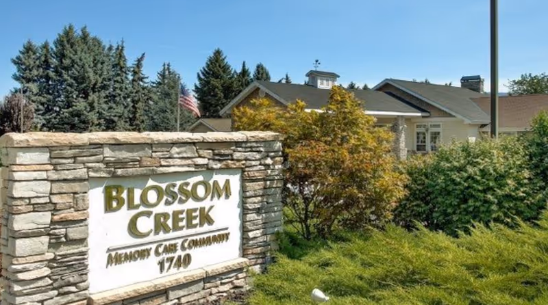 Stone sign for Blossom Creek Memory Care Community with landscaping and building behind.