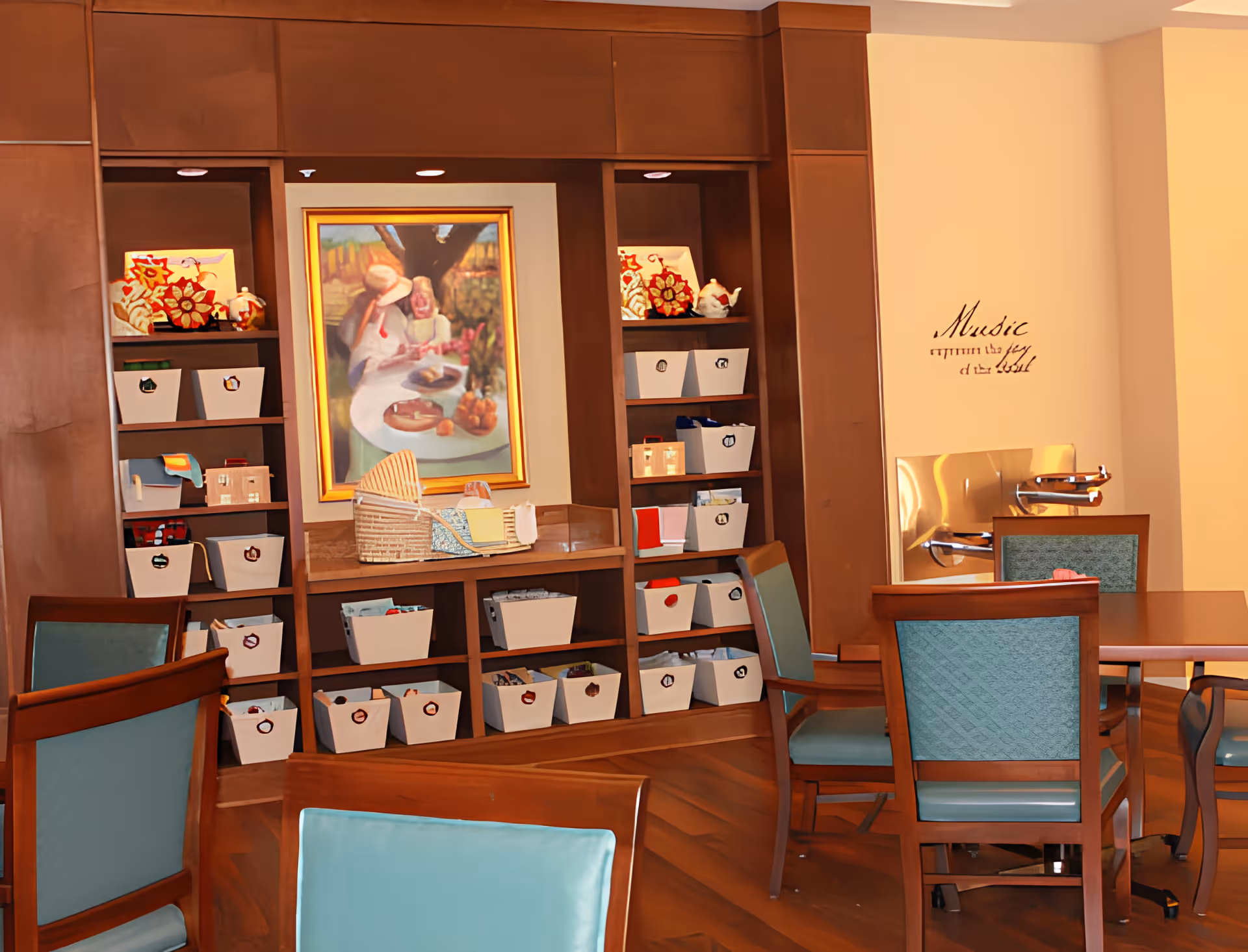 A cozy interior room with wooden shelves filled with white storage bins, a framed painting of two people at a table, and a wooden table surrounded by chairs with teal cushions. On the wall, there is a decorative quote that reads 'Music within the joy of the soul.'
